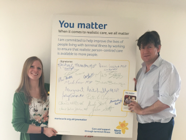 Alex and a representative from Marie Curie holding a poster between them.